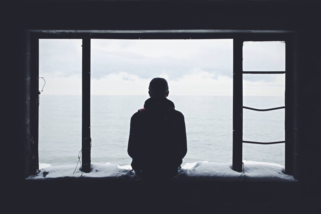 A guide to the staff redundancy process for employers 3 A dark silhouette from behind of a man sat on a bench alone looking out to sea. The man has short hair and is wearing a coat