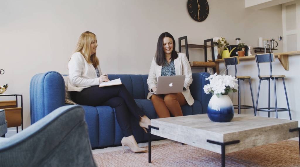 HR Director Sian Whelan and Recruitment Director Siobhan Collyer sat on a blue sofa both wearing business wear. Siobhan is looking at an Apple Macbook whilst Sian has a notebook. HR Director Sian Whelan and Recruitment Director Siobhan Collyer sat on a blue sofa both wearing business wear. Siobhan is looking at an Apple Macbook whilst Sian has a notebook.